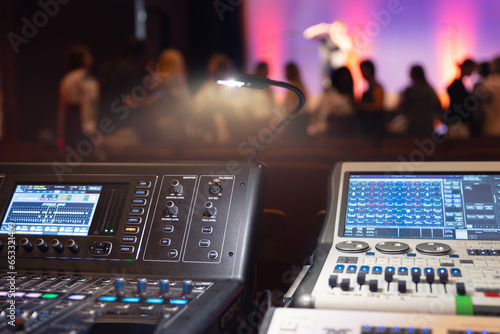 Live theater concert show sound video music control console with scene lights background. Sound engineer mixer soundboard equipment with many knobs, buttons, faders, equalizer screen and light