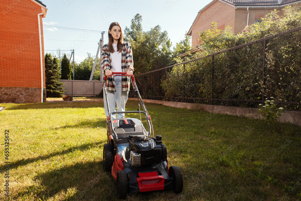 Female gardener working in autumn, cutting grass in backyard. Concept of gardening, work, nature. Housework, gardening and country life. Home garden grass cutting woman mowing with lawn mower. Female gardener working in autumn, cutting grass in backyard. Concept of gardening, work, nature. Housework, gardening and country life. Home garden grass cutting woman mowing with lawn mower.