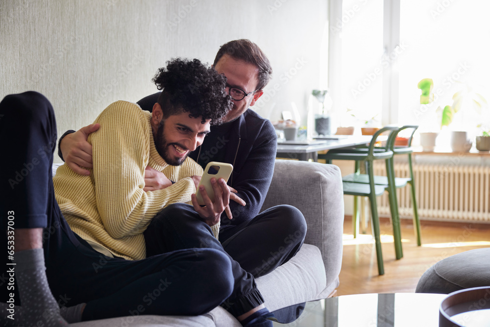 Gay couple relaxing on sofa at home and using phone Gay couple relaxing on sofa at home and using phone