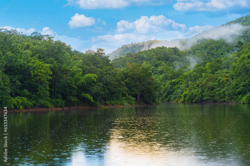 A small lake in Thailand surrounded by mountains with lush green forest and mist.