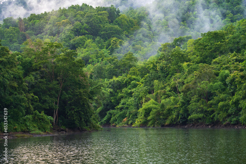 A small lake in Thailand surrounded by mountains with lush green forest and mist.