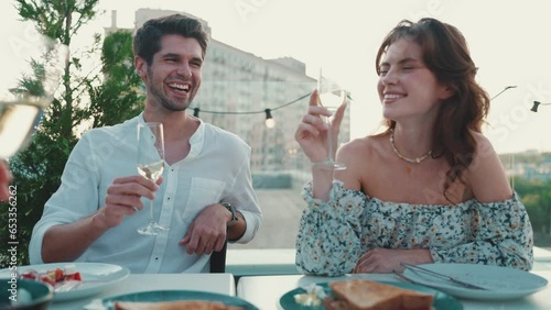 Smiling couple clinking glasses while celebrating with friends on restaurant balcony