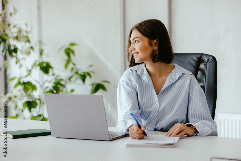 Woman with papers in an office working at her desk with a laptop in front of her. Woman with papers in an office working at her desk with a laptop in front of her.