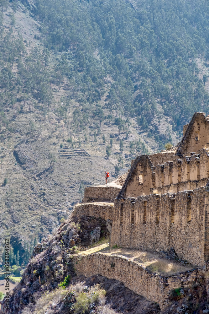 A man on his back with a red backpack standing at an ruin of Incas