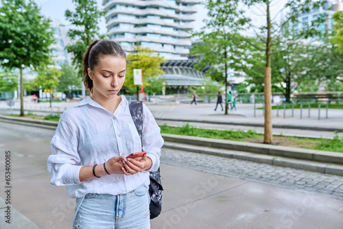 Portrait of young teenage female student with smartphone, on street of city