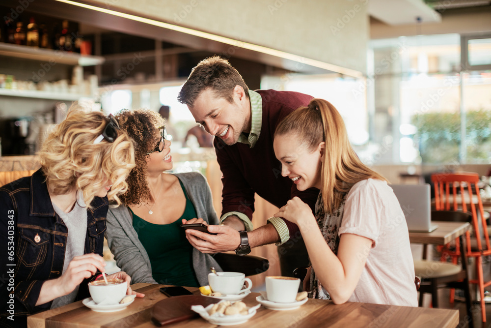 Group of young and diverse friends using a smartphone while having coffee together in a cafe or bar