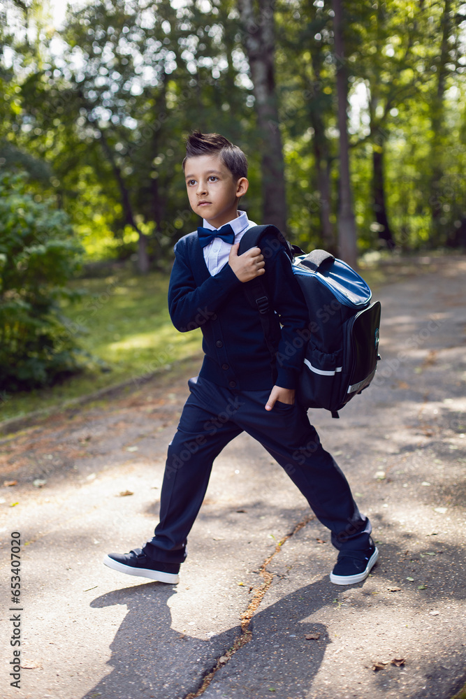 portrait firstgrader boy in a uniform with a bow tie and a backpack is