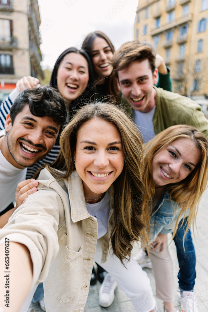 Fototapeta premium Vertical shot of young millennial people taking selfie with phone at city street. Youth community and friendship concept.
