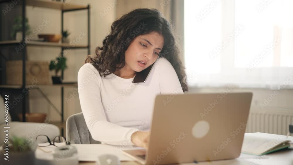 Nervous stressed young woman freelancer typing quickly on laptop computer hurry up scream and warning about deadline while having working call conversation by smartphone at light home workplace Nervous stressed young woman freelancer typing quickly on laptop computer hurry up scream and warning about deadline while having working call conversation by smartphone at light home workplace