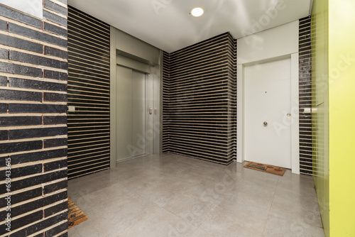 Landing of residential building with metal elevator, gray stoneware floors and black brick walls