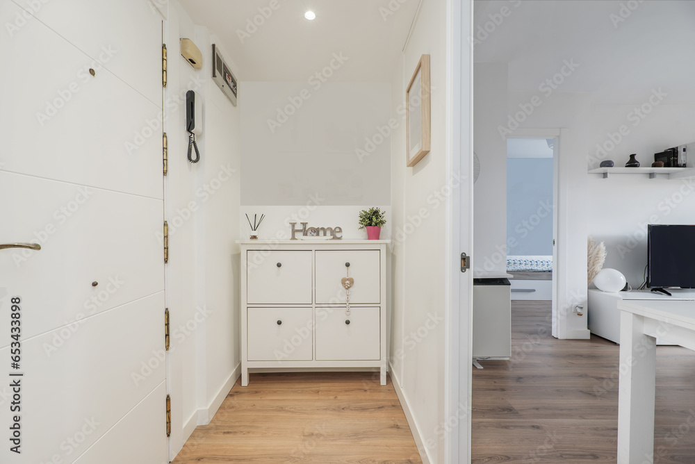 Fototapeta premium Hallway of a home with a white drawer unit, access door from the street and access to another room with white furniture