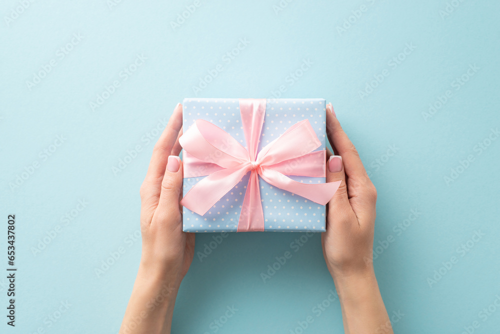 Wrapped with love: woman's hands from first person top view hold a pastel blue gift box, featuring polka dots and a pink ribbon bow, on a pastel blue canvas, leaving room for your text or advert Wrapped with love: woman's hands from first person top view hold a pastel blue gift box, featuring polka dots and a pink ribbon bow, on a pastel blue canvas, leaving room for your text or advert