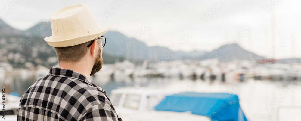 Banner rear view millennial man wearing hat with yachts and marina background with copy space and empty place for advertising