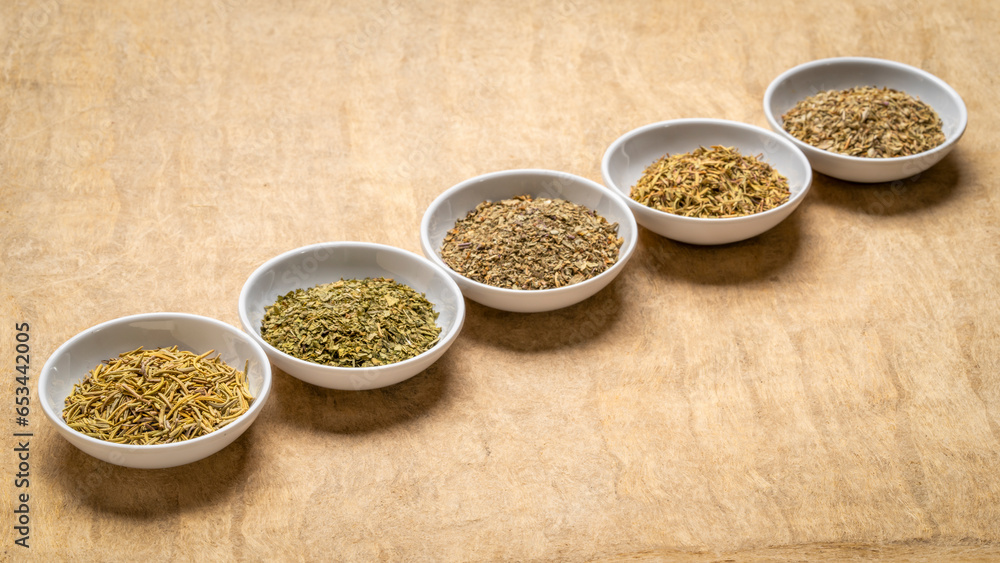 herb spices - dried leaves of parsley, rosemary, thyme, basil and oregano, collection of small ceramic bowls on a textured bark paper herb spices - dried leaves of parsley, rosemary, thyme, basil and oregano, collection of small ceramic bowls on a textured bark paper