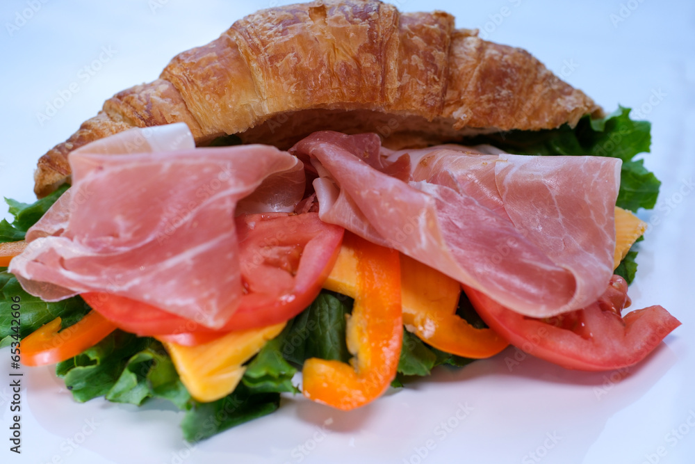 Delicious croissant with ham and cheese placed on white plate. Croissant with prosciutto and herbs Delicious croissant with ham and cheese placed on white plate. Croissant with prosciutto and herbs