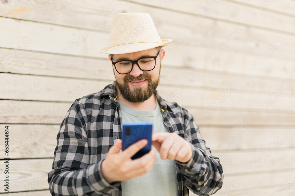 Millennial male tourist use smartphone during summer city break over wooden wall with copy space - technologies and social media app concept Millennial male tourist use smartphone during summer city break over wooden wall with copy space - technologies and social media app concept