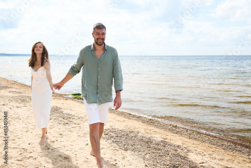 A photoshoot of a Happy caucasian couple walking holding hands on Baltic Sea sandy beach