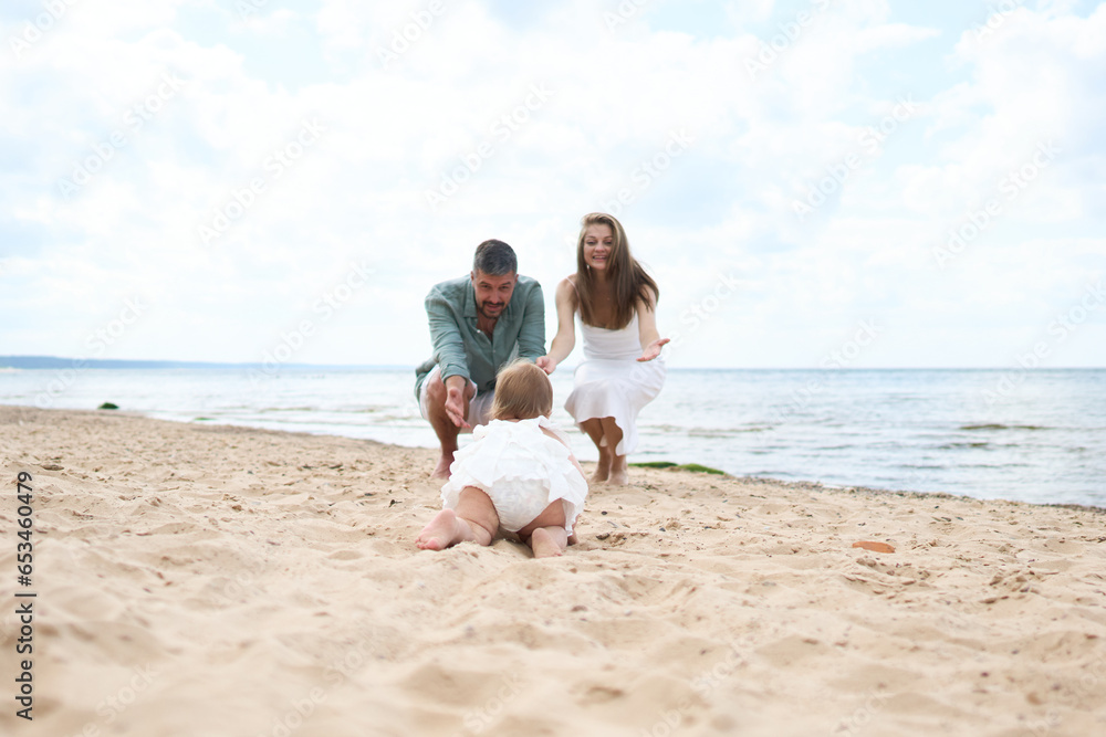 A photoshoot of happy parents playing with their 1 year old girl playing on sand near the beach
