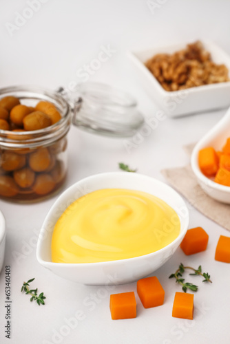 Bowl with tasty cheddar cheese sauce, thyme and olives on white background