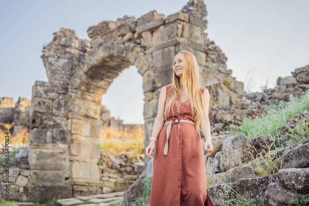 Fototapeta premium Woman tourist explores Aspendos Ancient City. Aspendos acropolis city ruins, cisterns, aqueducts and old temple. Aspendos Antalya Turkey. turkiye