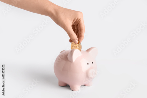 Female hand putting bitcoin into piggy bank on white background