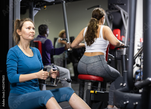 Woman is engaged in a simulator with horizontal weights in the gym