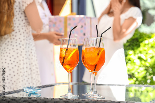 Young women with glasses of tasty aperol spritz on table greeting friend in cafe, outdoors