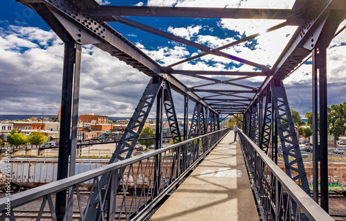 A man on a pedestrian bridge over a railyard in Laramie, Wyoming USA with the town and storm clouds in the background.