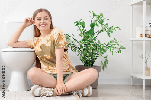 Young woman sitting near toilet bowl in restroom