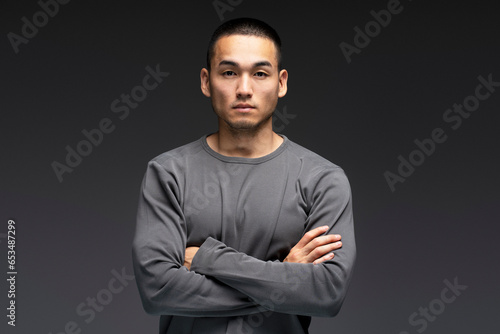 Serious, emotionless young Asian man standing isolated on black background, looking at camera