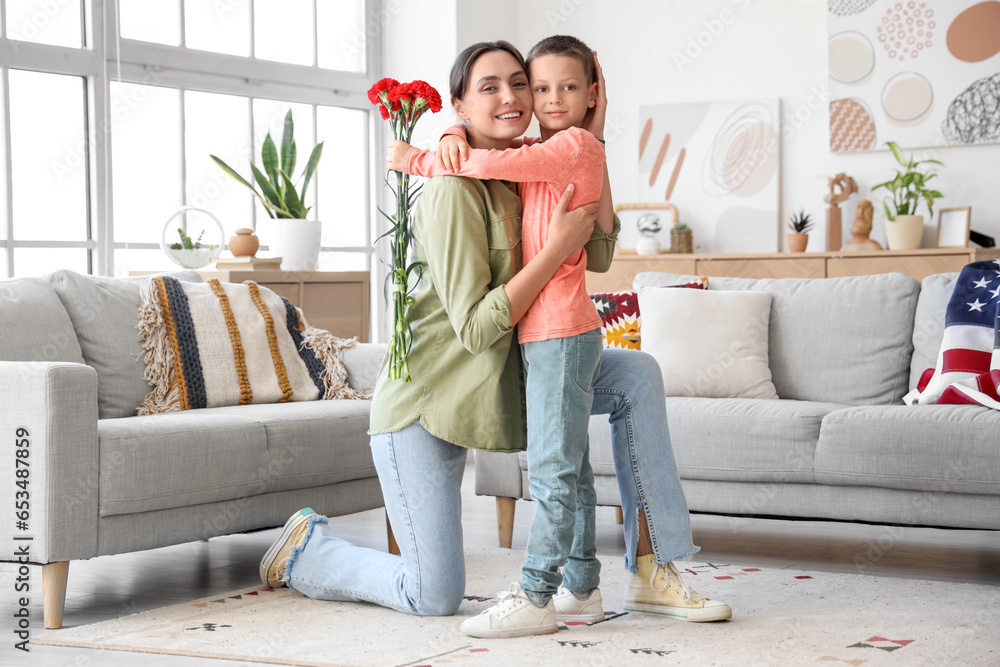 Obraz premium Little boy with carnation flowers hugging his mother at home. Veterans Day celebration