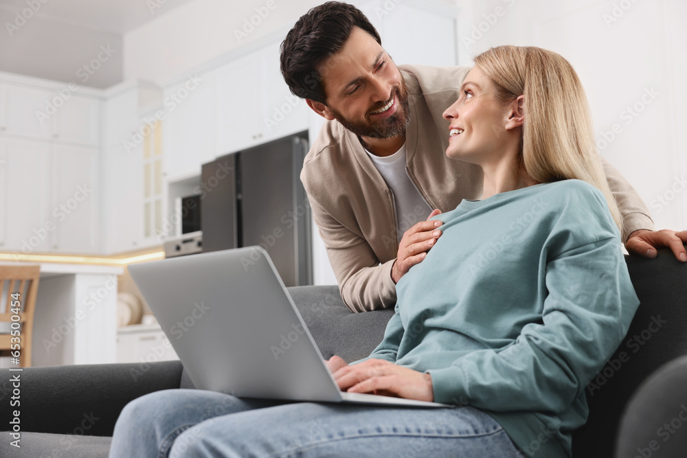 Happy couple using laptop on sofa at home, low angle view Happy couple using laptop on sofa at home, low angle view