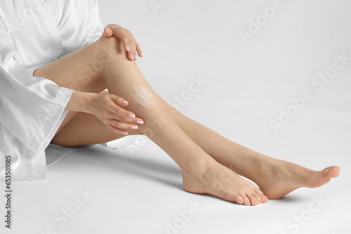 Woman applying body cream onto her smooth legs on white background, closeup © New Africa