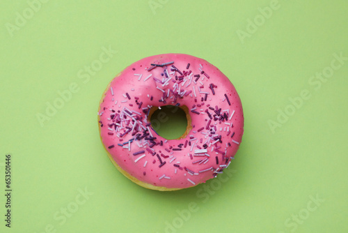 Glazed donut decorated with sprinkles on green background, top view. Tasty confectionery
