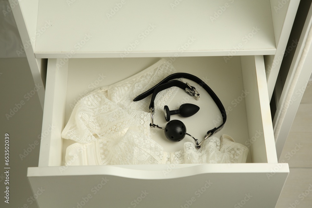 Anal plug, ball gag and women's underwear in open drawer of nightstand indoors, closeup. Sex toys - obrazy, fototapety, plakaty 