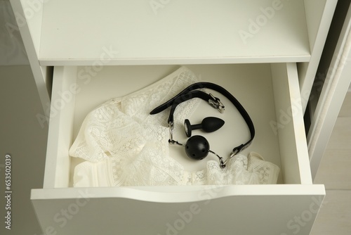 Anal plug, ball gag and women's underwear in open drawer of nightstand indoors, closeup. Sex toys