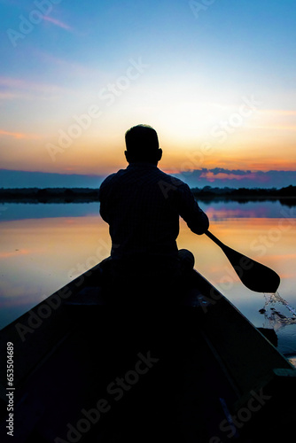 Silhouette of a man paddling canoe at dusk calm water © PhotoSpirit