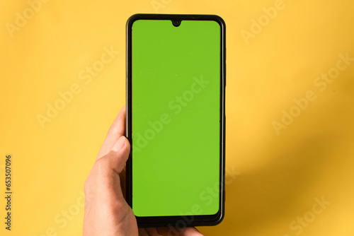 Obraz na plátně hand holding modern mobile phone green screen isolated on yellow background