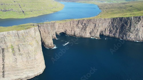 Aerial shot of Lake Sorvagsvatn meander and Traelanipa cliff with hikers on its edge. Faroese landscape photo