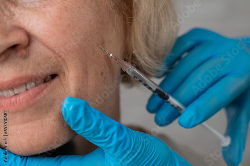 Doctor makes beauty injections in the face of an old caucasian woman. 