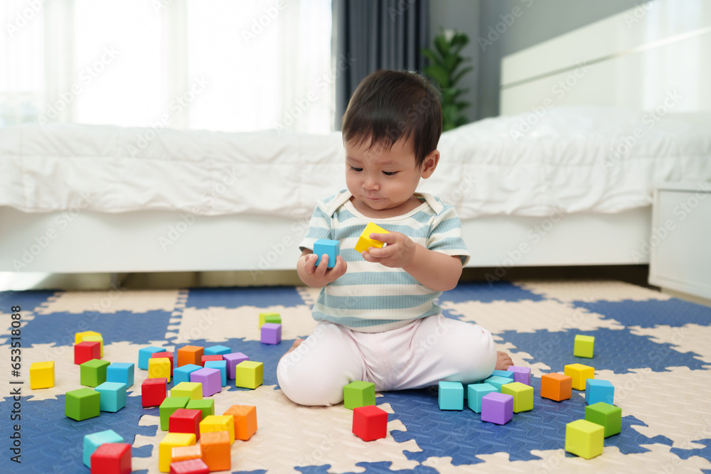 happy infant baby playing wooden block toy on jigsaw mat in bedroom happy infant baby playing wooden block toy on jigsaw mat in bedroom