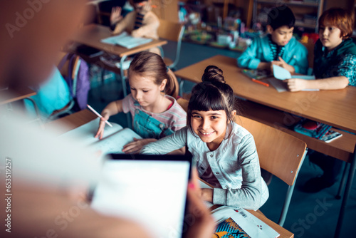 Young African American teacher looking at the work of her students in a elementary school classroom photo