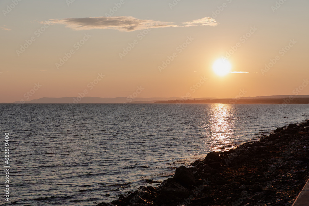 vue du bord d'une plage rocailleuse en bord de mer lors d'un coucher de soleil d'été