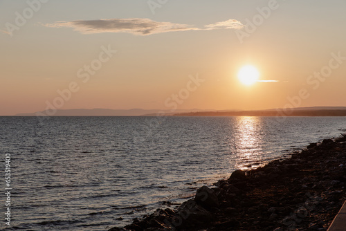 vue du bord d'une plage rocailleuse en bord de mer lors d'un coucher de soleil d'été © Veronique