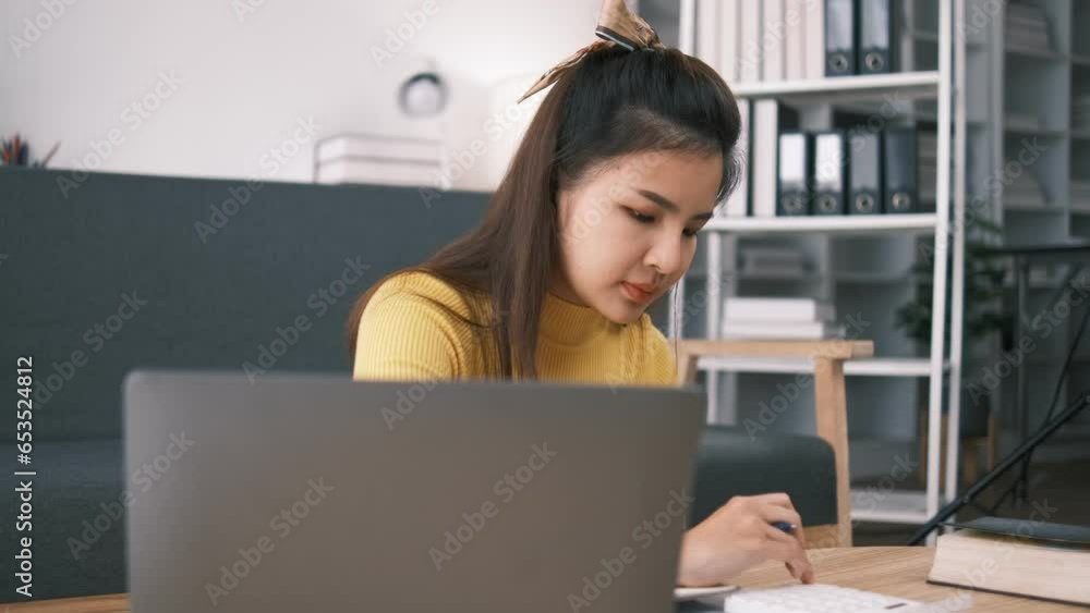 Happy Asian woman sits in her living room calculating taxes and managing household expenses. Happy Asian woman sits in her living room calculating taxes and managing household expenses.