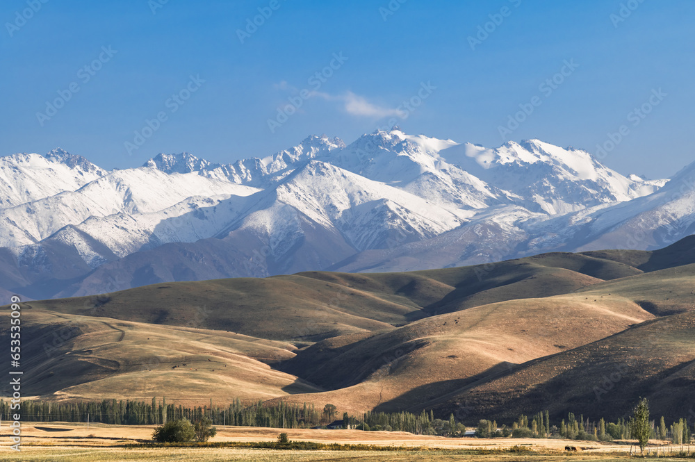 Mountain hills with snow-capped peaks and blue sky. Mountains and village life in Kyrgyzstan.