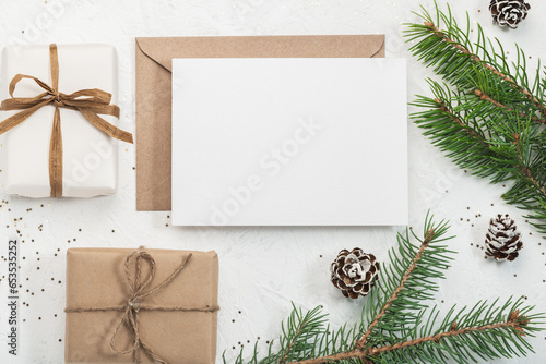 Two Christmas gift boxes, an envelope made of craft paper and a blank form, ribbons and scissors on a white background and fir branches. Christmas greeting card. Boxing Day.