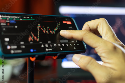 An Investor analysis the stock market exchange from the candlestick graph. Trader at home office trading on computer and using mobile phone. Financial and broker agent investment concept.