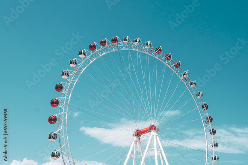 Red and white booths on top a white Ferris wheel against the sky.