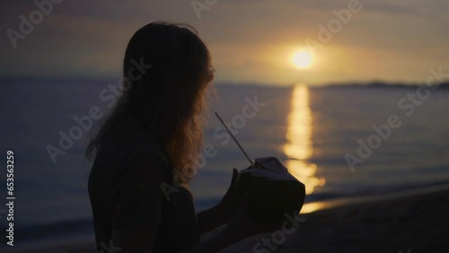 Women enjoying a fresh coconut at a beautiful beach at sunset photo